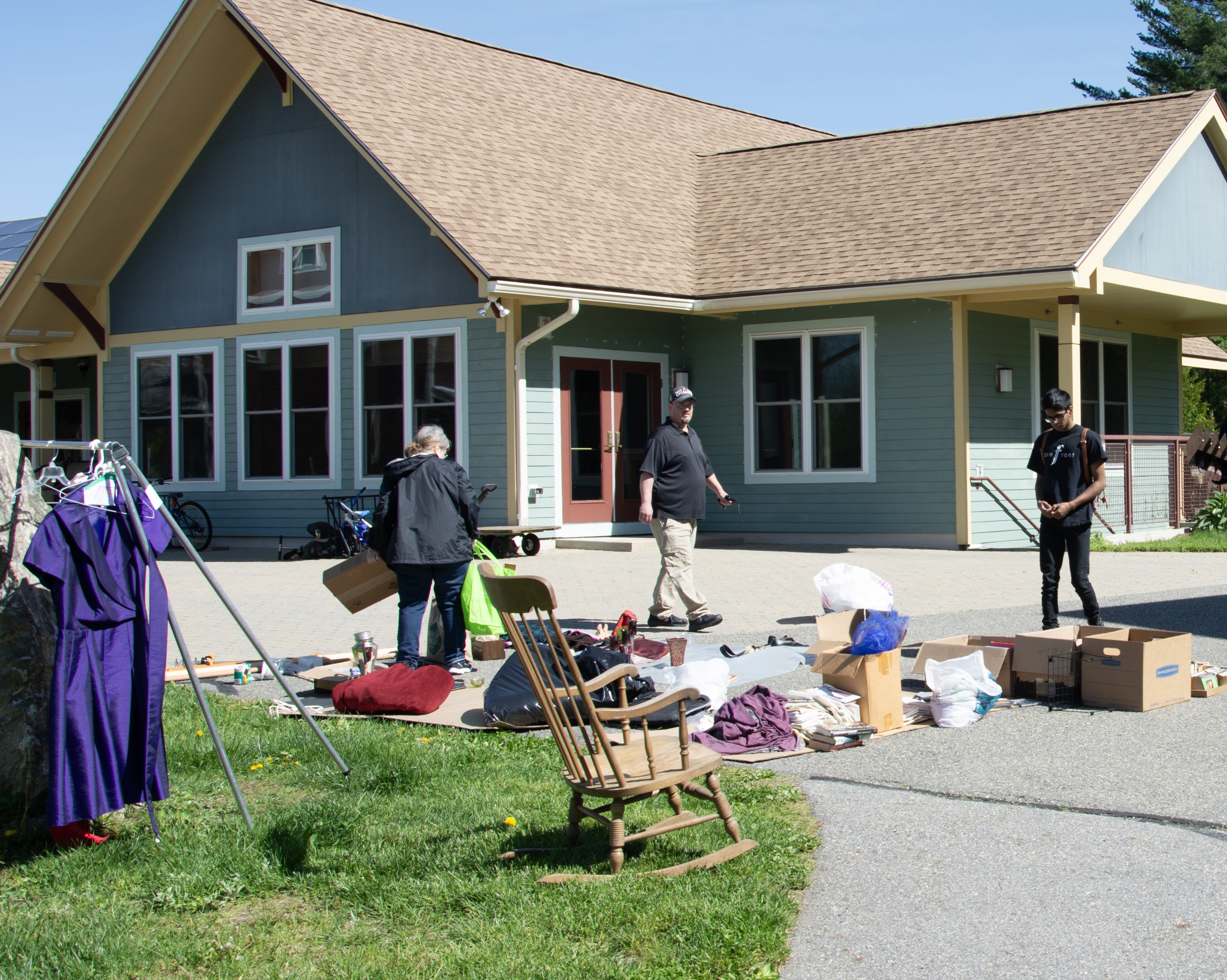 a rocking chair, a rack of clothes, and a variety of small household items laid out on the common house patio
