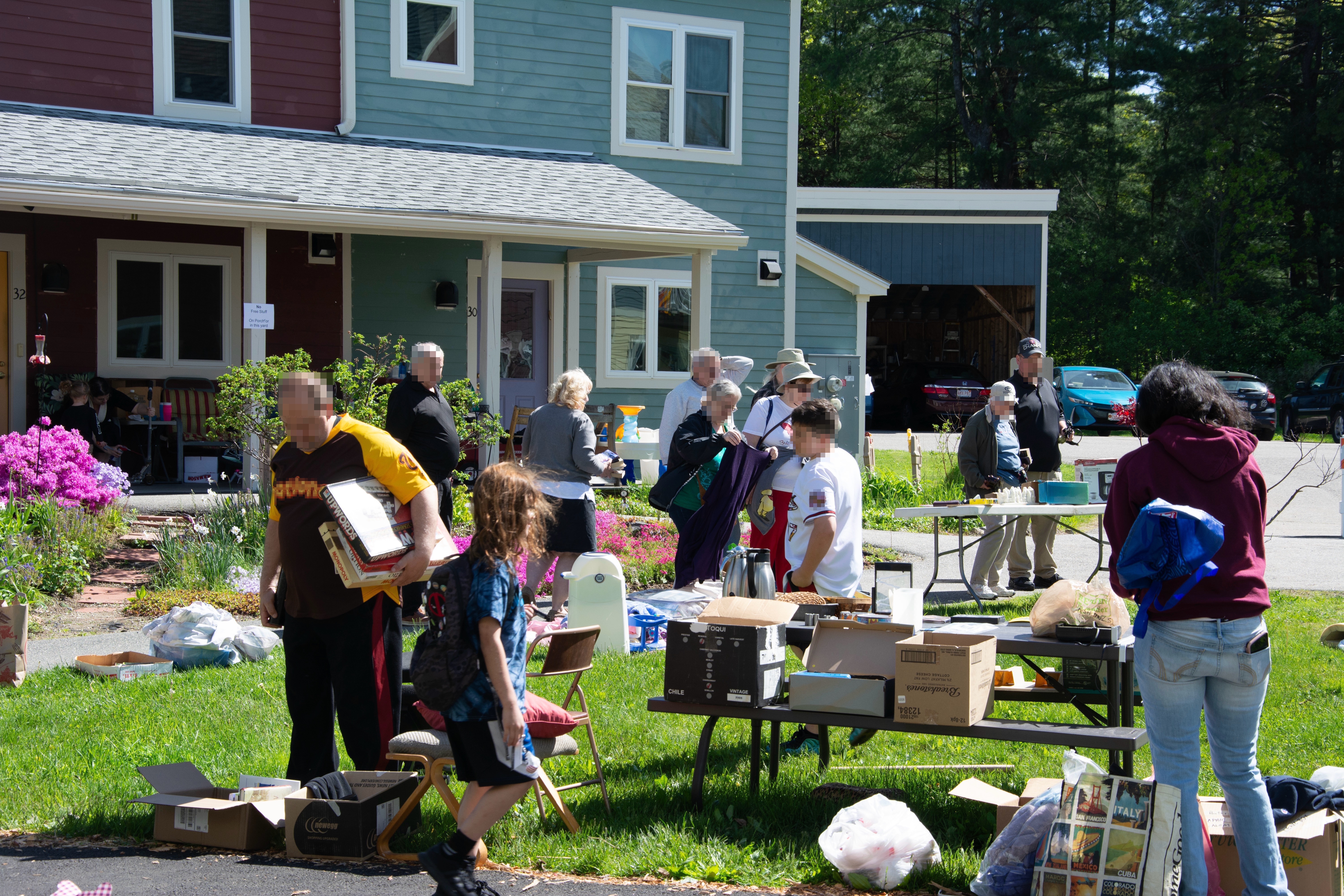 several adults and children explore giveaway items on tables and tarps on the grass
